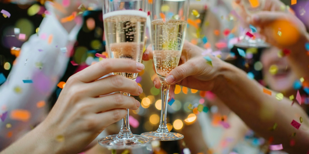 Des mains trinquent avec des flûtes de champagne sous des confettis colorés